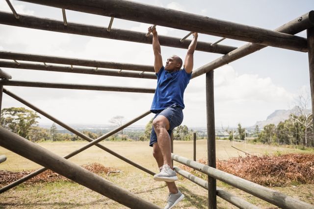 This image shows a fit man climbing monkey bars during an obstacle course in a boot camp. Ideal for use in fitness and exercise promotions, outdoor training programs, boot camp advertisements, and motivational content related to physical challenges and endurance.