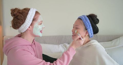 Diverse friends applying facial masks at home spa night, sharing self-care moment