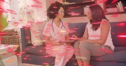 Nurse consulting patient during home visit on couch using tablet, stethoscope, cozy living room