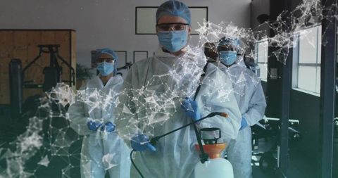 Sanitation team wearing full ppe disinfecting gym with sprayer and digital network overlay