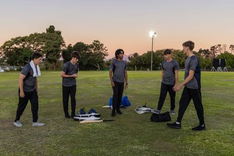 Diverse male teammates gathering on field at dusk wearing training gear and duffels