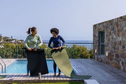 Diverse women rolling out yoga mats on coastal pool deck preparing outdoor workout