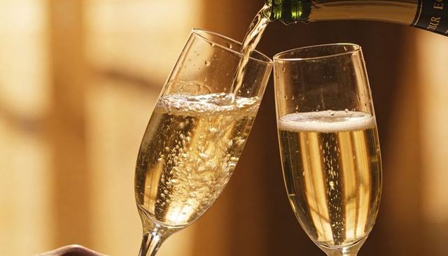 Pouring champagne into two flutes with bubbles and warm golden bokeh for celebration