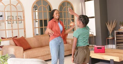 African american mother and daughter high-fiving in cozy living room, bonding moment