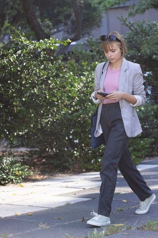 Young professional walking while texting on smartphone in sunlit urban park