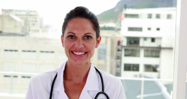 Female doctor smiling at workplace with stethoscope and white coat. Useful for health services, medical promotional materials, healthcare articles, and wellness programs.