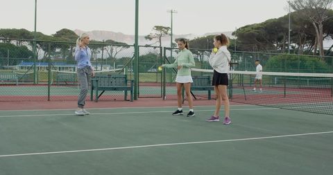 Female coach coaching players practicing tennis drills on outdoor court near mountains