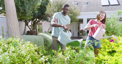 Diverse Couple Joyfully Watering Backyard Garden