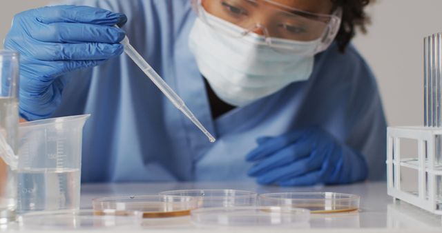 Female scientist wearing lab coat, safety goggles, and face mask conducting research in laboratory setting. She is using a pipette to add liquid to petri dishes. Can be used for topics like scientific research, lab safety, medical advancements, biotechnology, and STEM education.