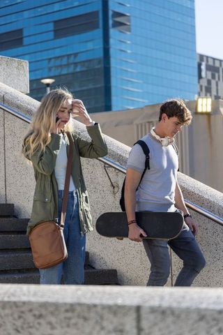 Teen friends walking down urban stairs carrying skateboard and using phone