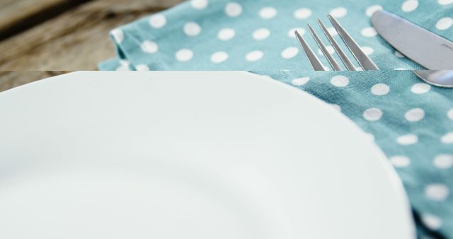 A white plate paired with a fork and knife rests on a polka-dotted napkin, with copy space. The setting suggests a casual dining atmosphere, ready for a meal to be served.