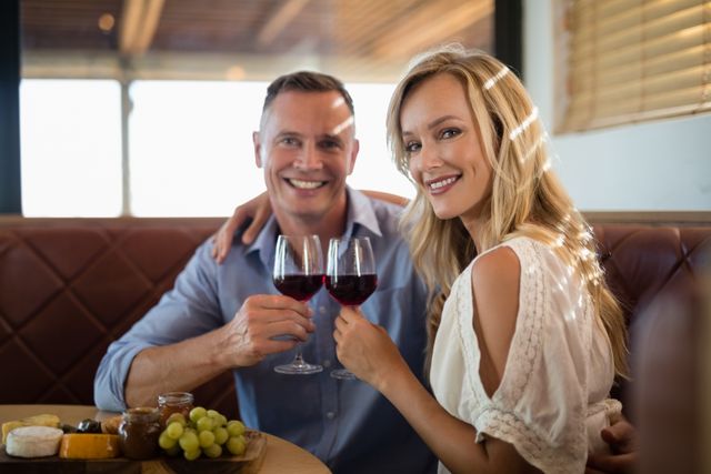 Happy couple toasting with wine while enjoying a meal in a restaurant. They are smiling and appear to be celebrating a special occasion. Ideal for use in advertisements, blogs, or articles about dining, relationships, celebrations, and lifestyle.