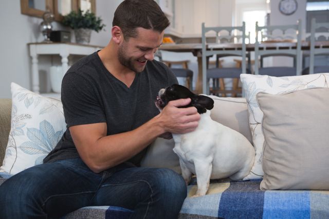 Man enjoying quality time with his French Bulldog in a comfortable living room. Perfect for themes of pet ownership, domestic life, relaxation, and human-animal bonding. Ideal for use in articles, blogs, and advertisements related to pets, home living, and lifestyle.