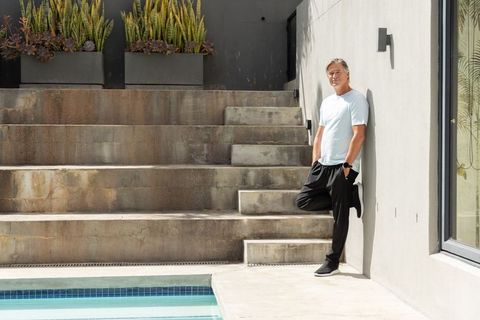 Mature man leaning poolside by terraced concrete steps, minimalist outdoor living