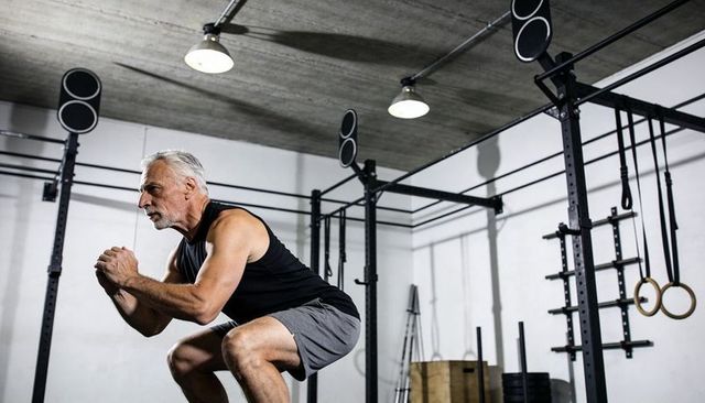Senior man performing deep squat in industrial gym with rings, rig and bodyweight training