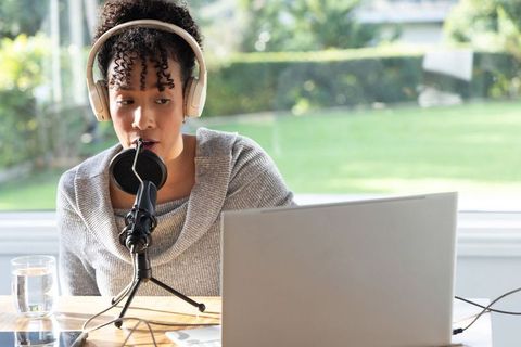 African american woman recording podcast at home office with headphones laptop microphone