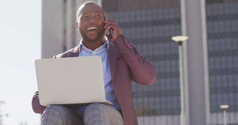 Smiling Professional Conversing on Smartphone While Using Laptop Outdoors