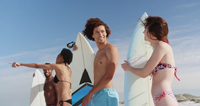 Diverse friends with surfboards enjoy a beach day. They share a moment of joy and anticipation for the surf ahead.