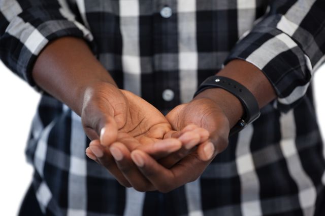 This image shows a man standing with his hands cupped together, wearing a plaid shirt and a black watch. It can be used to represent concepts such as offering, giving, receiving, or asking for help. Suitable for use in articles, blogs, advertisements, or social media posts related to charity, support, or human connection.