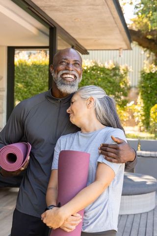 Sunlit mature couple embracing on patio after yoga holding colorful mats