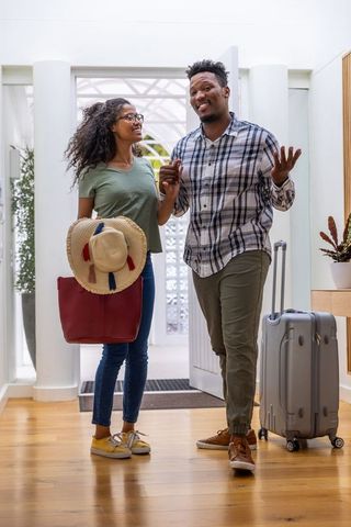 Young couple arriving home with luggage and straw hat at front door