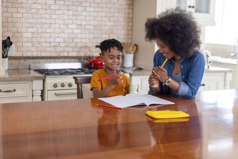 African american mother teaching son at kitchen table using colored pencils for homework