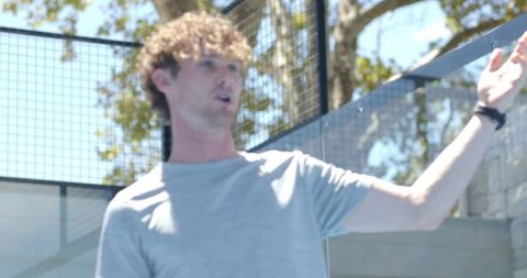 Young man speaking and gesturing on modern sunlit terrace with glass panels and mesh fence