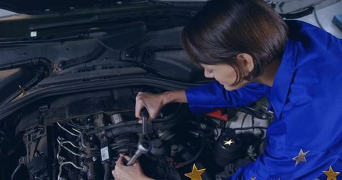 Female mechanic tightening engine bolt with socket wrench in garage with gold stars detail