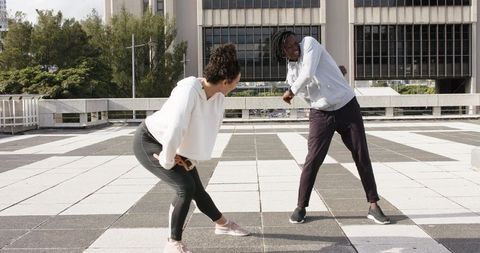 Diverse pair stretching on urban rooftop with checkered tile floor wearing workout gear