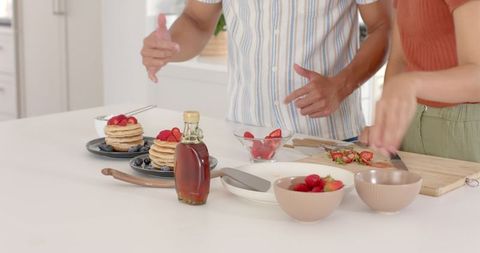 Couple garnishing pancake stacks with fresh fruit in modern kitchen