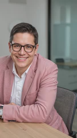 Vertical corporate intro video smiling professional leaning on desk in pink blazer