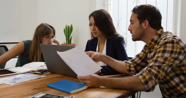 Young Caucasian woman and man review documents in an office. They are focused on work, collaborating in a bright, professional setting.