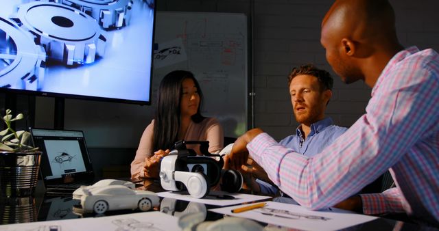 Three professionals are collaborating on a robotic design project in a modern office. The team includes a female and two males of different ethnicities, discussing their work around a table with robotic models and design sketches. Ideal for use in content related to teamwork, engineering, technology development, and innovative projects.