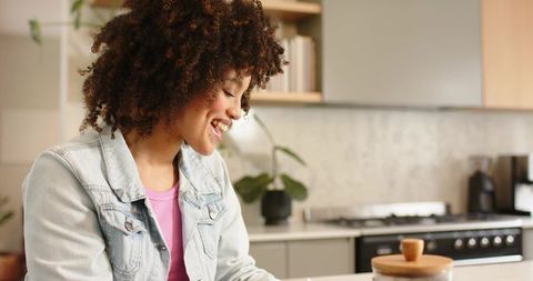 Smiling young woman in modern kitchen preparing coffee next to wooden jar