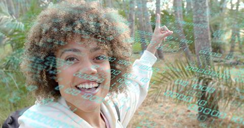 Smiling woman pointing at forest trail with glowing binary code overlay, ar nature concept