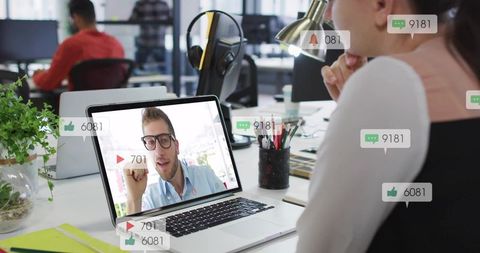 Woman watching remote video call on laptop with live chat and like notifications in open office