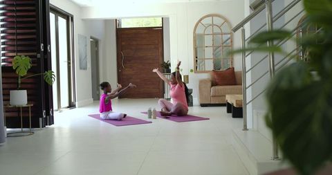 African mother and daughter practicing yoga and stretching together in modern home entryway