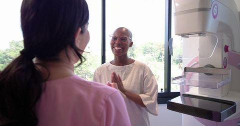 Woman Smiling Before Mammogram Screening While Tech Preparing Equipment in Clinic