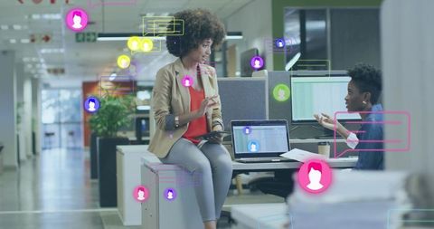 Two colleagues collaborating at open-plan desk with laptop, digital avatars, teamwork