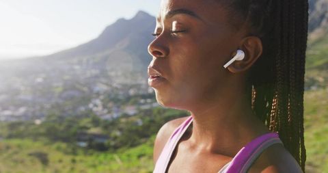 Sunlit athlete pausing to breathe with earbuds on hilltop during outdoor workout