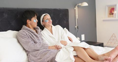Couple relaxing on bed in plush robes with eye patches enjoying romantic spa night
