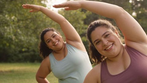 Plus-size women stretching and smiling together in park during outdoor side-stretch routine