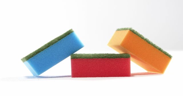 Three colorful sponges are stacked in a playful, uneven manner against a white background, with copy space. Their bright colors and simple composition make this image ideal for topics related to cleaning, household chores, or organization.