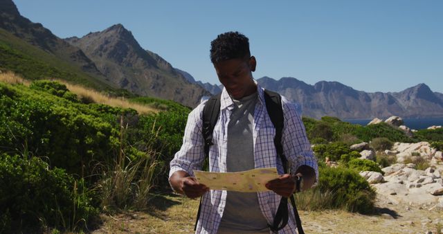 African american man hiking reading a map in coastal countryside. fitness training and healthy outdoor lifestyle.