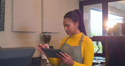 African American Barista Using Tablet Behind Sunlit Modern Coffee Bar Counter