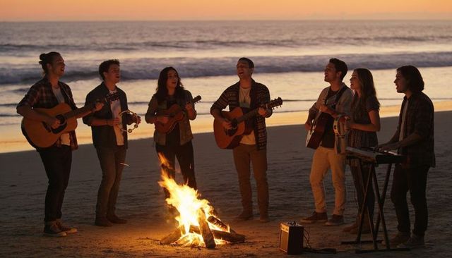 Sunset beach band singing and playing acoustic guitars around bonfire at dusk