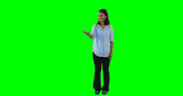 Woman standing against green screen background, wearing business casual attire, making a gesturing hand. Ideal for use in business presentations, educational videos, advertisements, and tutorials where adding custom backgrounds or graphics is required.