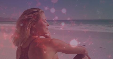 Woman relaxing on seaside shoreline with windblown blonde hair and pink dreamy bokeh