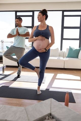 Pregnant Friends Practicing Yoga Tree Pose in Sunlit Living Room