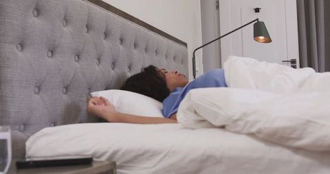African american woman sleeping under white duvet in minimalist bedroom, tufted headboard